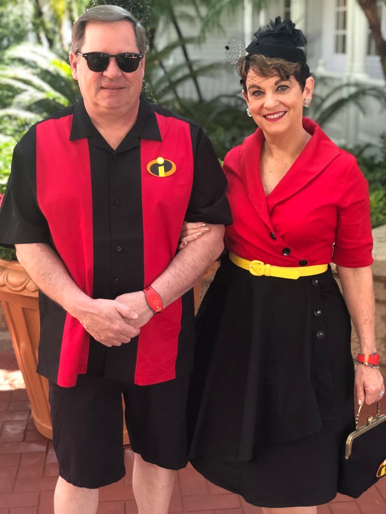Jane Treacy and her husband smile. Both of them are dressed in red, black, and yellow, with the theme of "The Incredibles."

