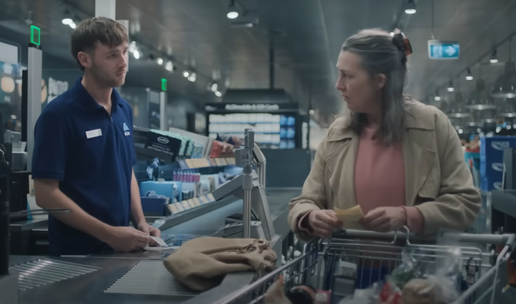 Woman and cashier stare sadly at each other in ALDI ad.