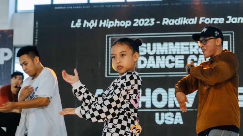 Nine-year-old Miyu Ananthamaya Pranoto looks stoic as she dances on stage with two young men dancing behind her.