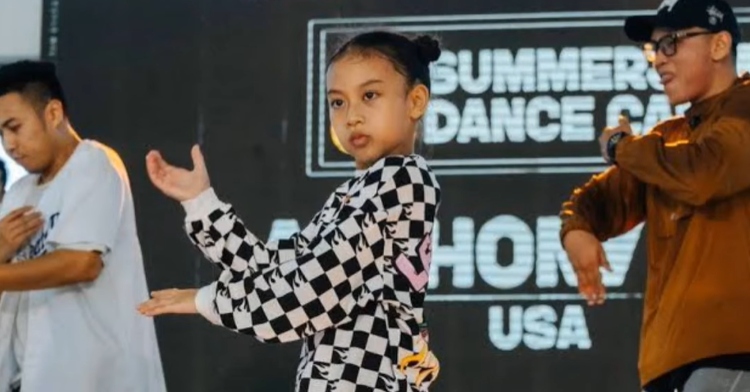 Nine-year-old Miyu Ananthamaya Pranoto looks stoic as she dances on stage with two young men dancing behind her.