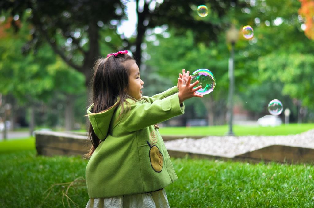 A toddler uses both hands to catch a bubble.
