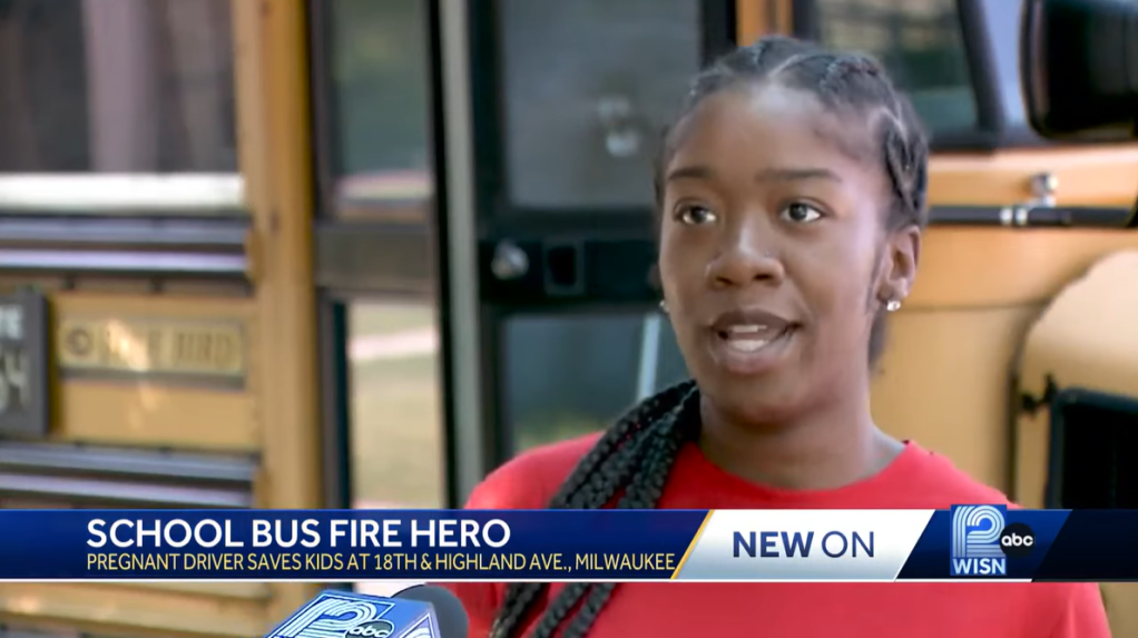 Imunek Williams talking to a new station while standing outside of a school bus.
