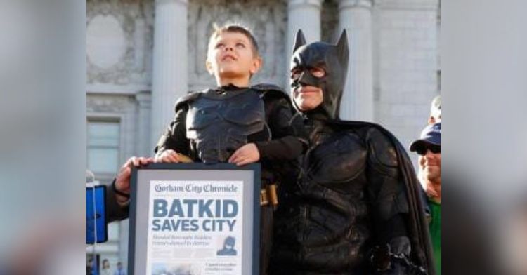 A young boy in a Batkid costume poses with Batman.