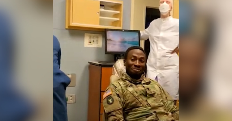 Soldier sits in a dental chair, smiling, as he reacts to the surprise he pulled off for his dental-worker wife.
