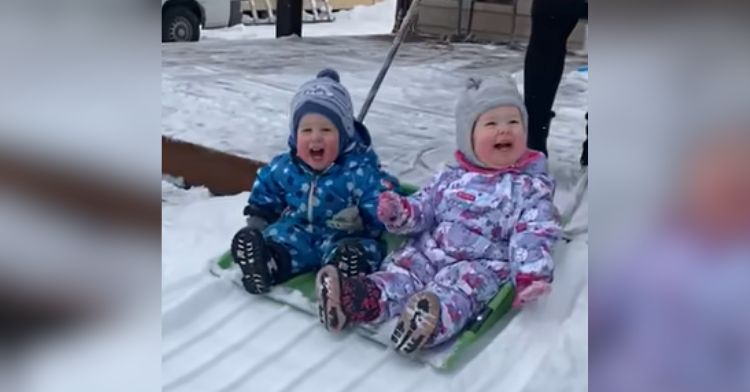 Laughing toddlers getting a ride down a snow slide.