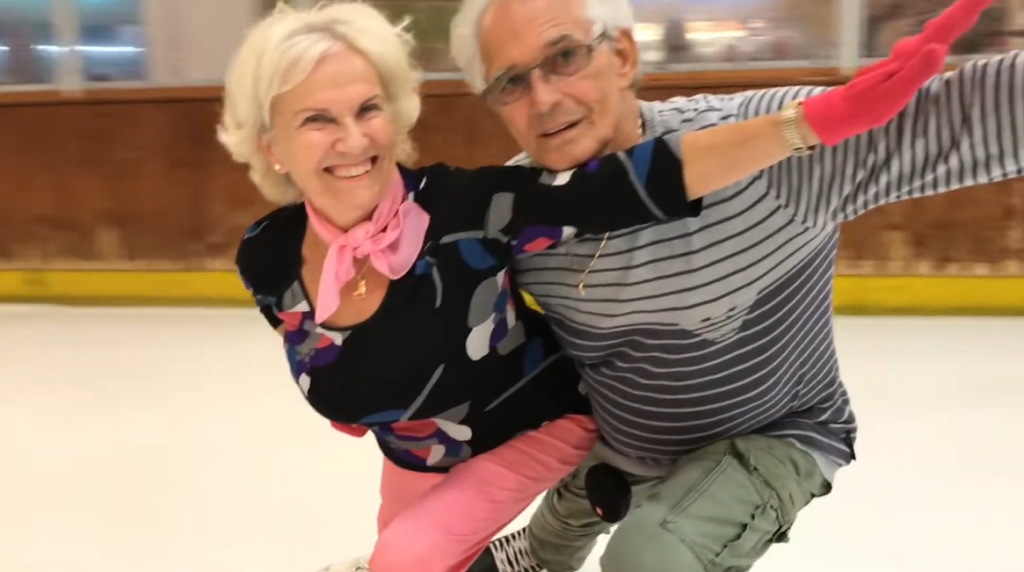 Close up of Mara Patai and László Gombos smiling as they skate, each of them with one arm stretched out.