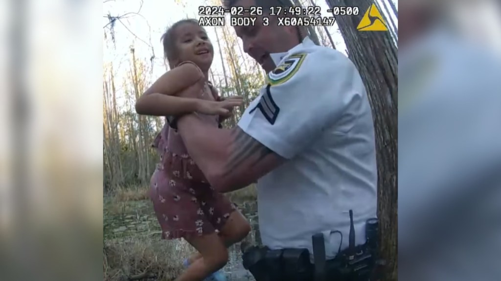 A police officer smiles as he lifts a missing girl from a swamp. She is also smiling.