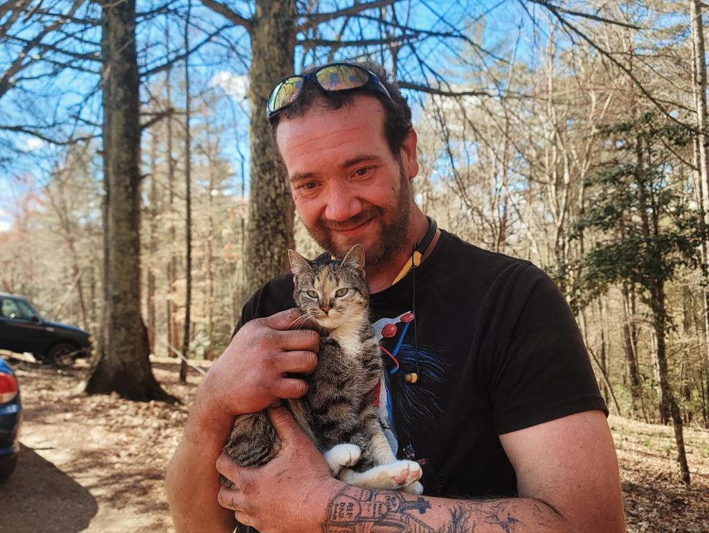 A man in the woods happily holds his rescued cat. 
