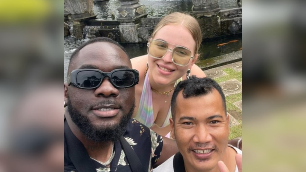 A local driver in Bali poses with sunglasses on with a couple that are tourists. They're all smiling for a selfie