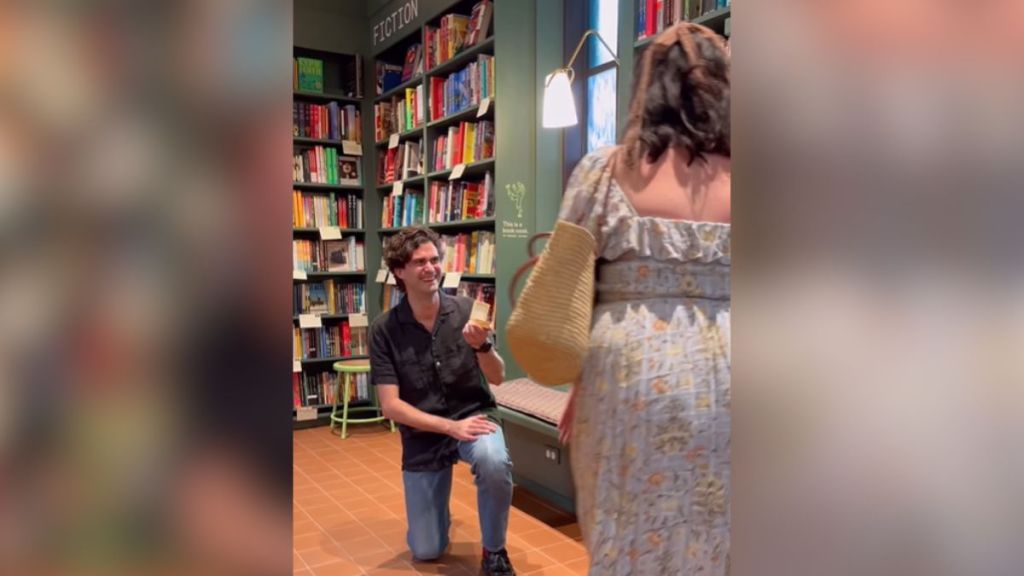 A man proposes to his girlfriend in a bookstore.