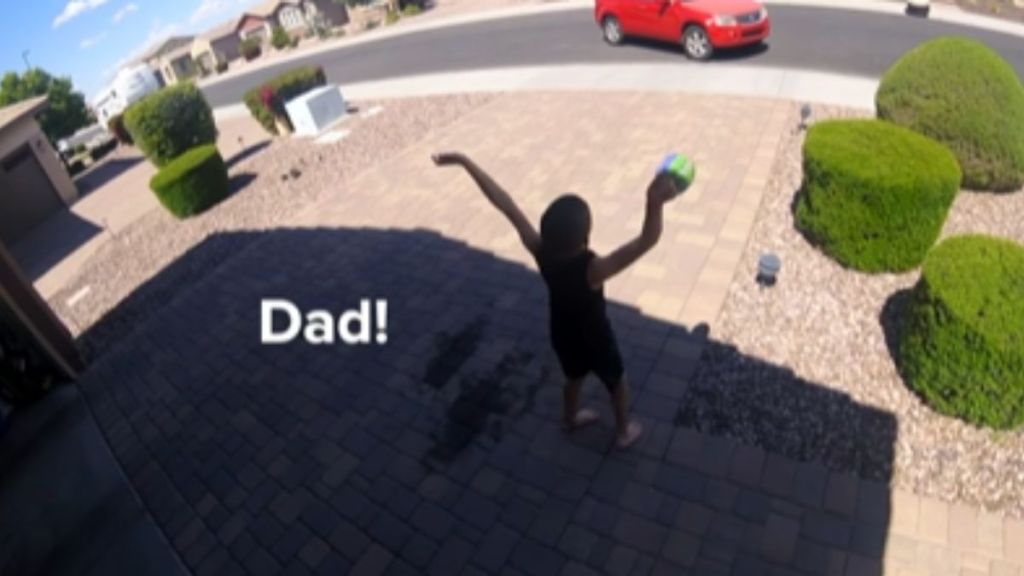 A son tries to wave down his dad, who is driving a red car.