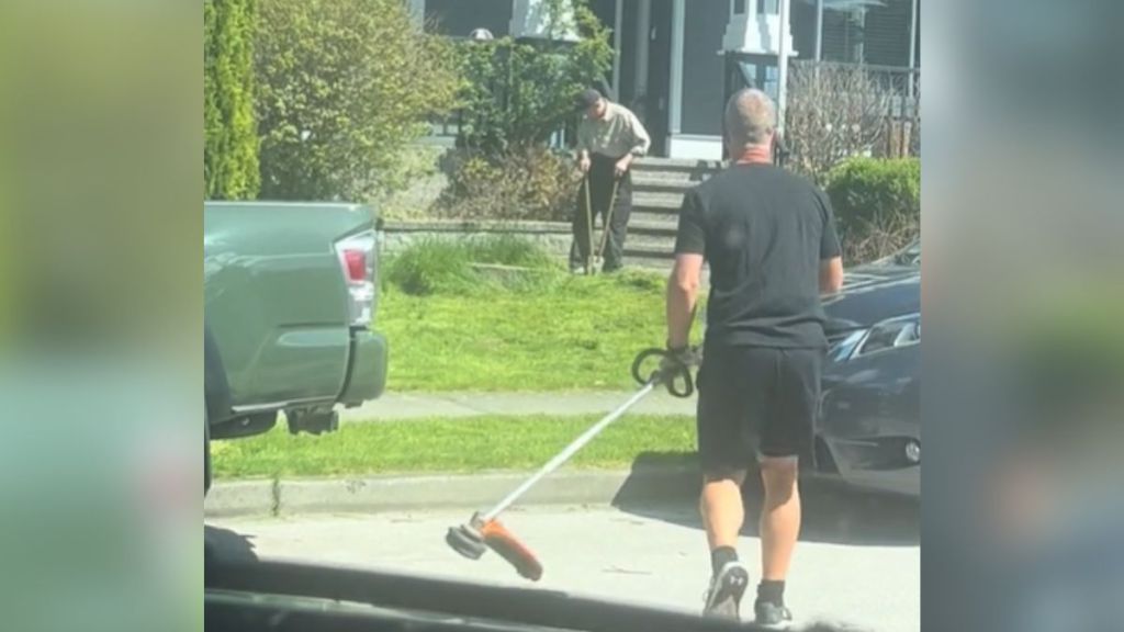 A man in black walks over to help an elderly man with his yard.