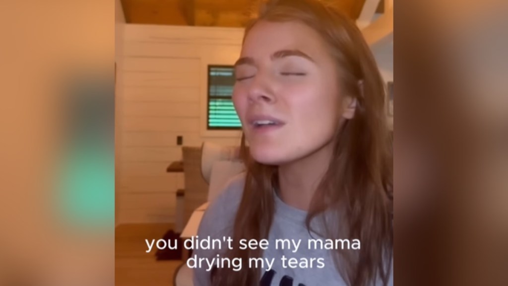 Close up of Emmy Russell singing passionately, eyes closed. Text on the image indicate what she's singing: you didn't see my mama drying my tears
