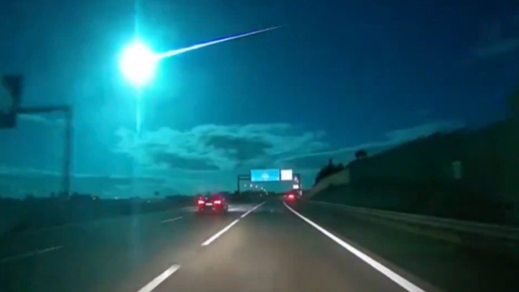 View from a car of a bright blue meteor shooting across the sky