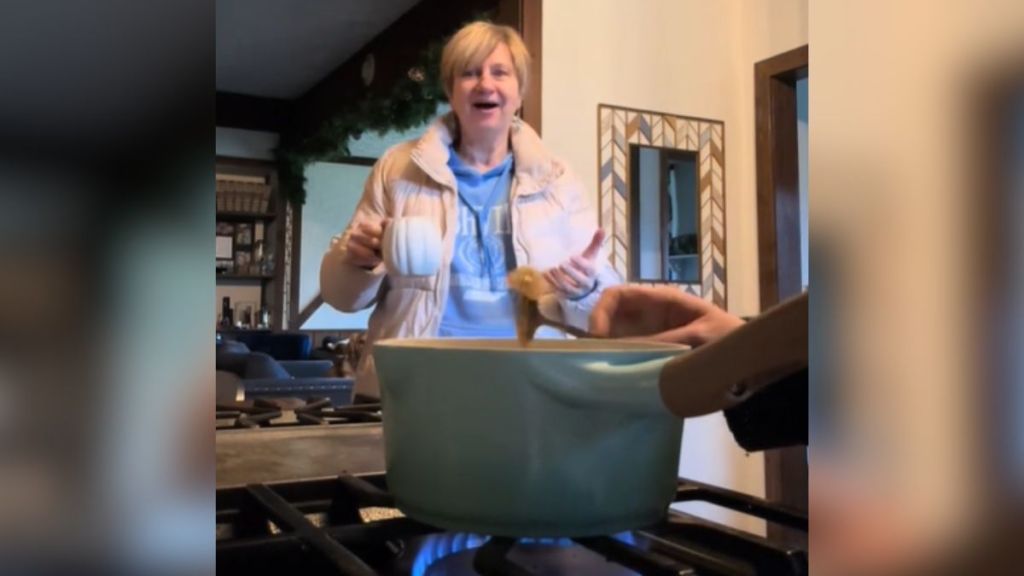 A grandma looks excited over a pot of something cooking on the stove.