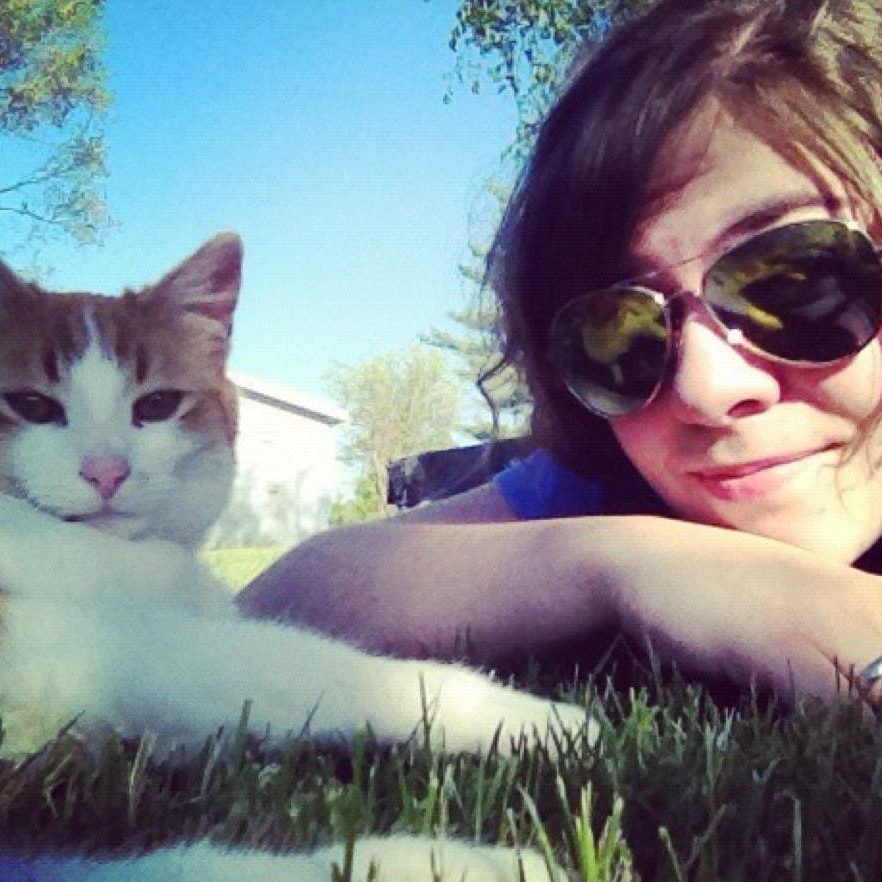 An orange and white cat next to a woman wearing sunglasses. 