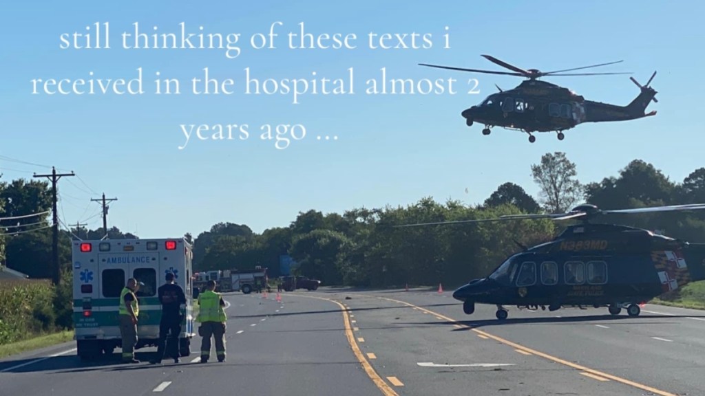 View of a road after an accident. There's an ambulance on the side of the road, a helicopter on the road, and a helicopter in the air. Text on the image reads: still thinking of these texts I received in the hospital almost 2 years ago...