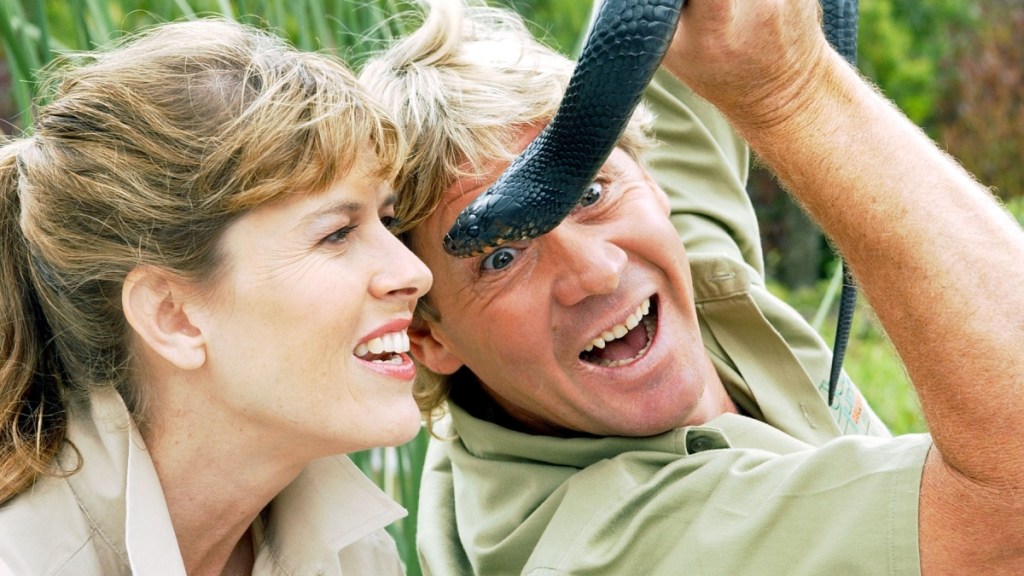 Terri Irwin looks at the snake Steve Irwin is holding up in front of her face. She's starting to smile and he has a huge grin on his face.
