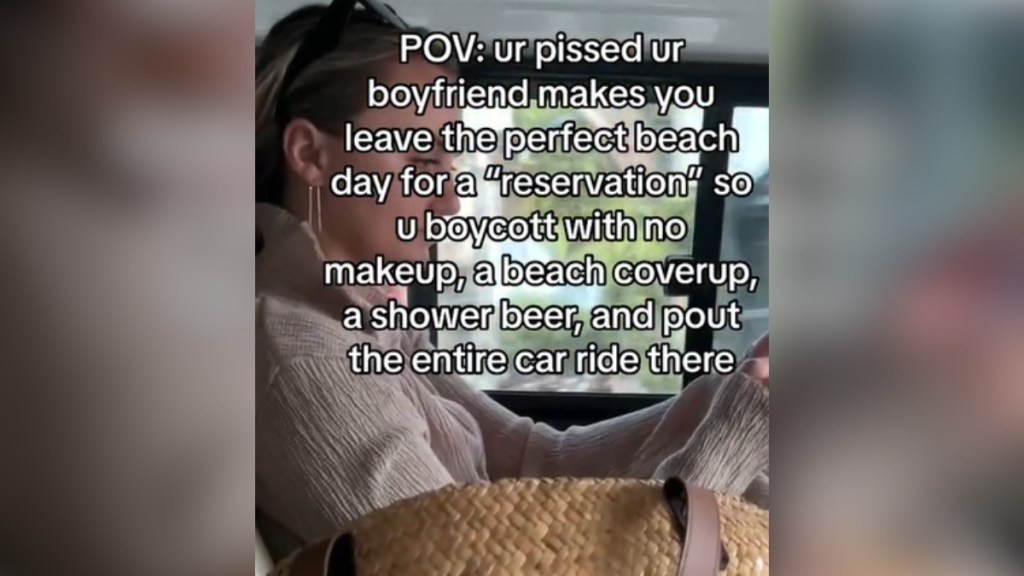 A woman sits in a car. She looks annoyed as she looks at her phone. Text on the image reads: POV ur pissed ur boyfriend makes you leave the perfect beach day for a "reservation" so u boycott with no makeup, a beach coverup, a shower beer, and pout the entire car ride there