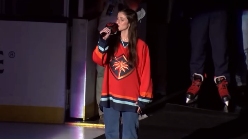 Abi Carter closes her eyes as she sings into a mic before a hockey game.