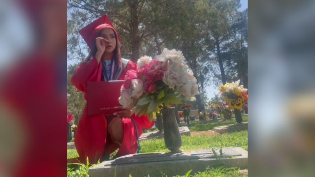 A graduate kneeling in front of a gravestone, crying.