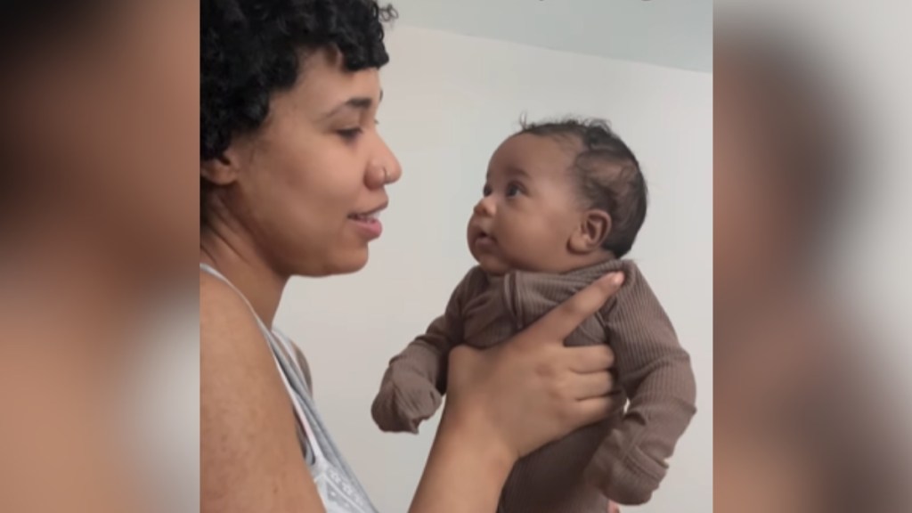 A mom sings as she holds her baby who is mesmerized staring at her, eyes wide.