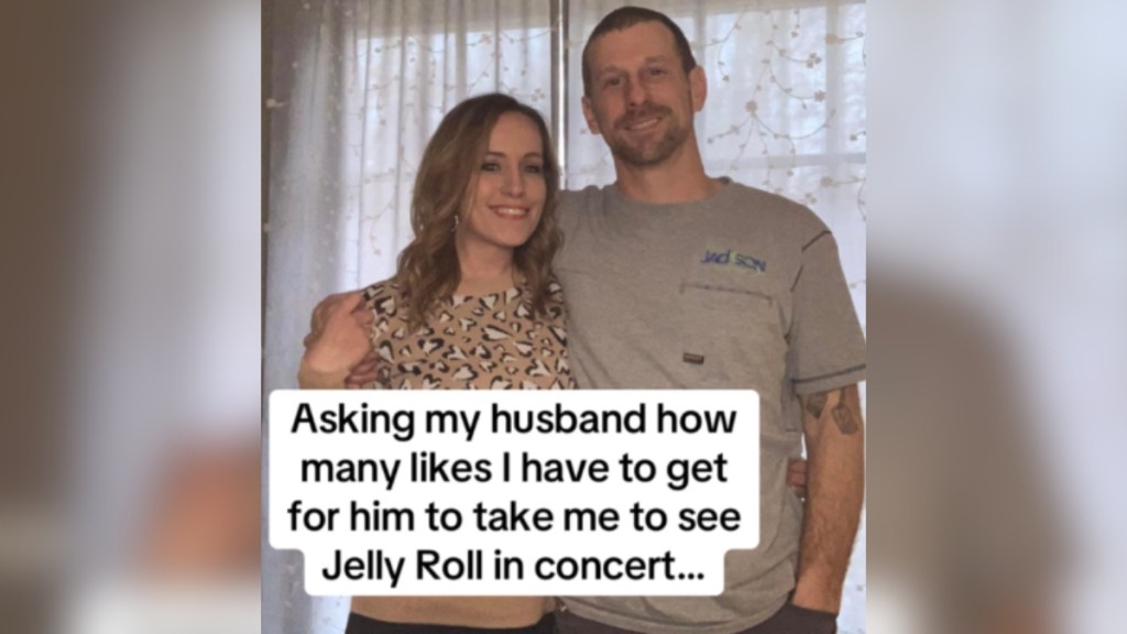 A man and woman smile as they post in front of a window. Text on the image reads: Asking my husband how many likes I have to get for him to take me to see Jelly Roll in concert...