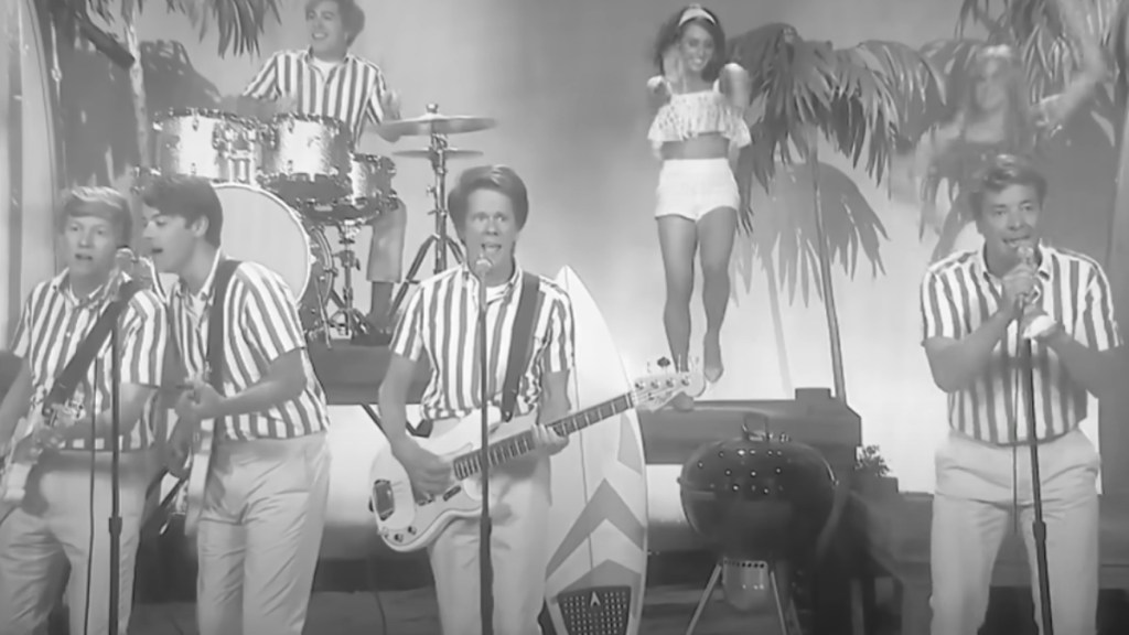 Black and white image of Kevin Bacon and Jimmy Fallon performing with others. Fallon sings as Bacon sings and plays guitar