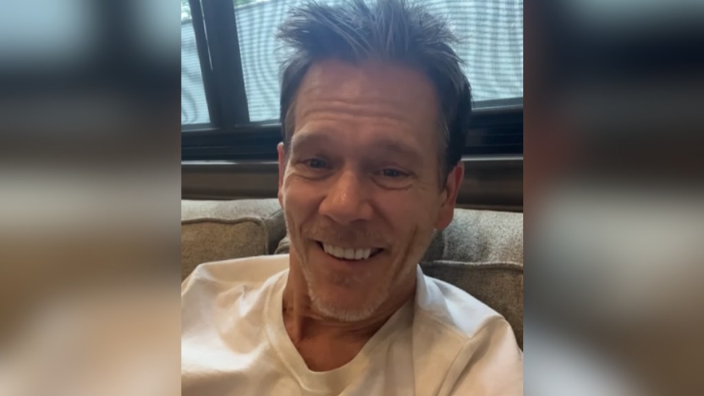 Close up of Kevin Bacon smiling from inside his trailer on set.
