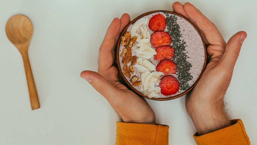 Someone wraps their hands around a bowl of food garnished by chia seeds. A spoon is also placed near the bowl