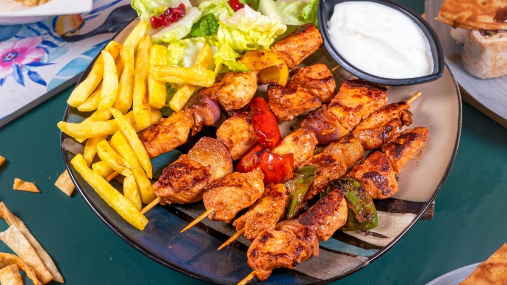 Plate full of fries, chicken kebabs, and a small bowl of dipping sauce