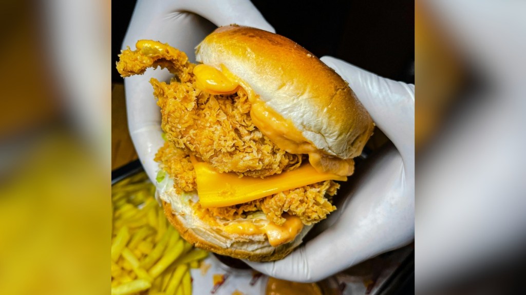 Close up of a fried chicken sandwich being held by someone wearing gloves