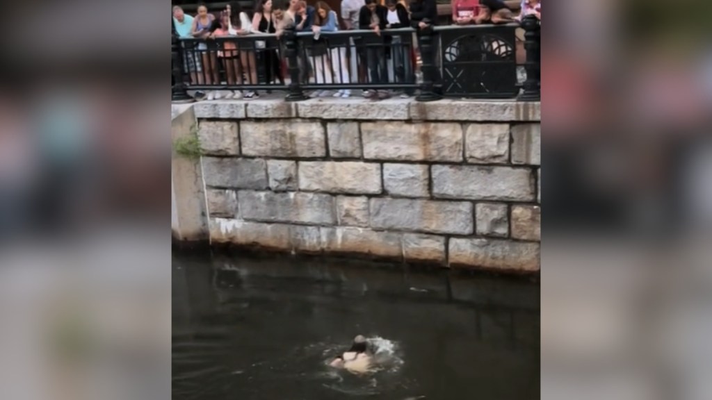 A woman swims in a river as a group of people watch her from above