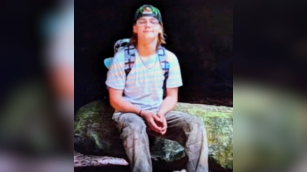 Lex Brown smiles, eyes closed, as he sits on a large boulder