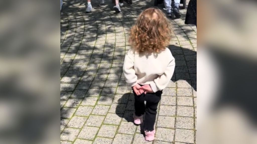 A little girl walking with her hands behind her back.