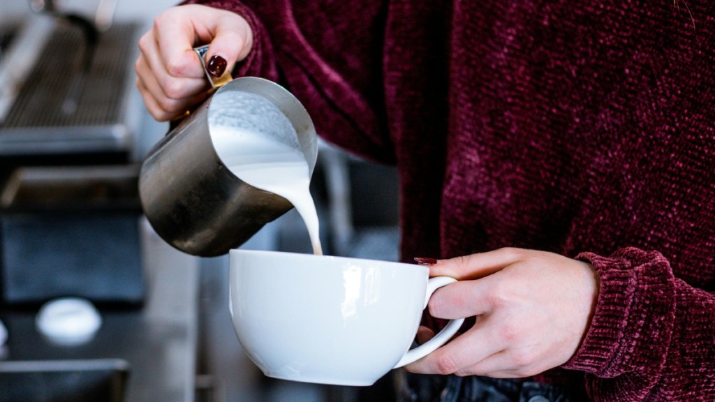 Close up of someone from around the shoulders down. They're pouring milk into a large cup