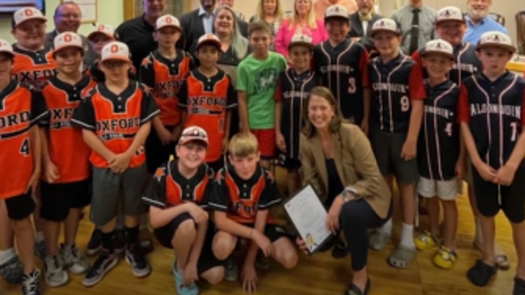 A woman smiles and poses with a Little League team