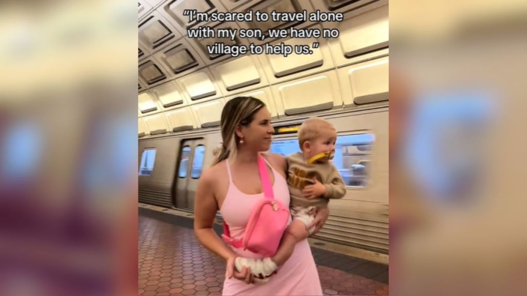 A woman in a pink dress holding a baby in a train station.