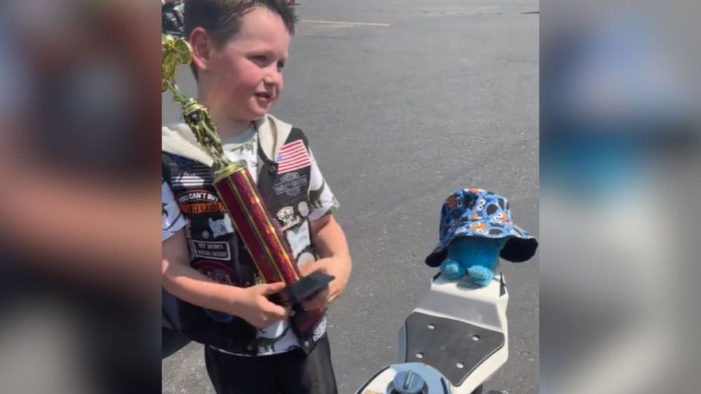 A little kid holding a trophy standing next to his bike.