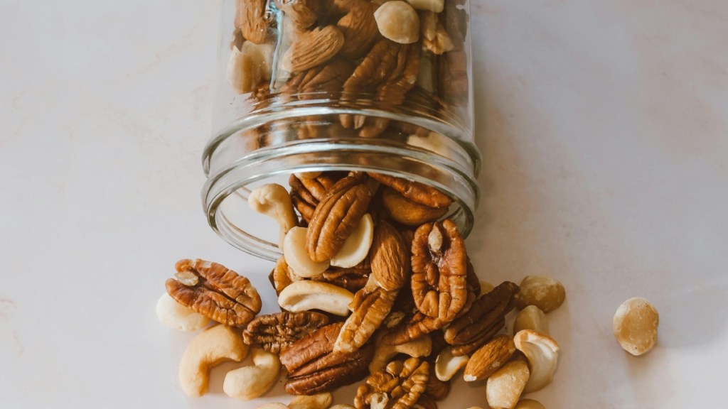 View of a clear container of mixed nuts partially poured out onto a table