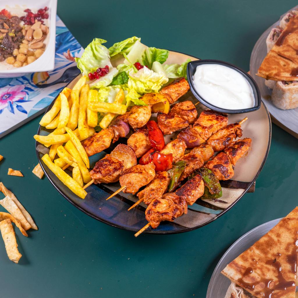 Plate full of fries, chicken kebabs, and a small bowl of dipping sauce