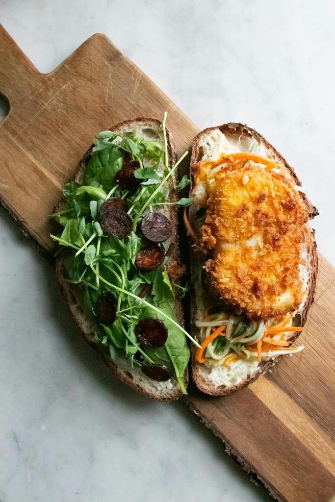 Close up of an open sandwich with veggies on one side and a breaded chicken cutlet on the other