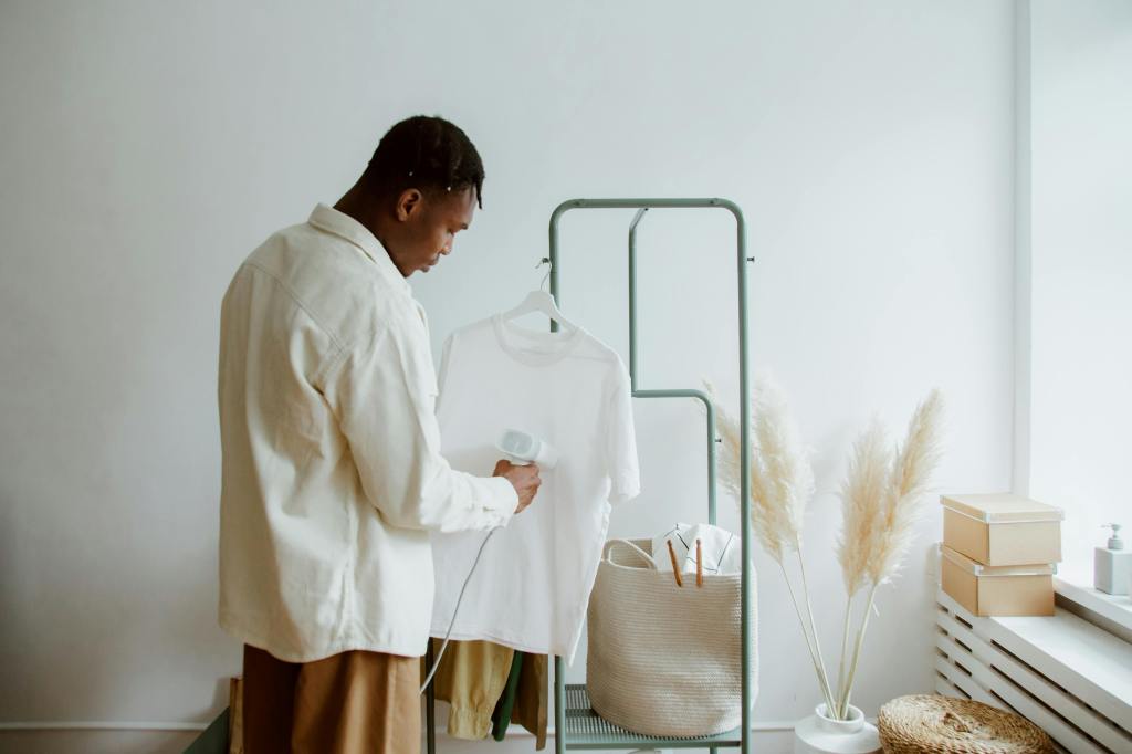 A man uses a small steam cleaner on a white shirt hanging from a mirror.