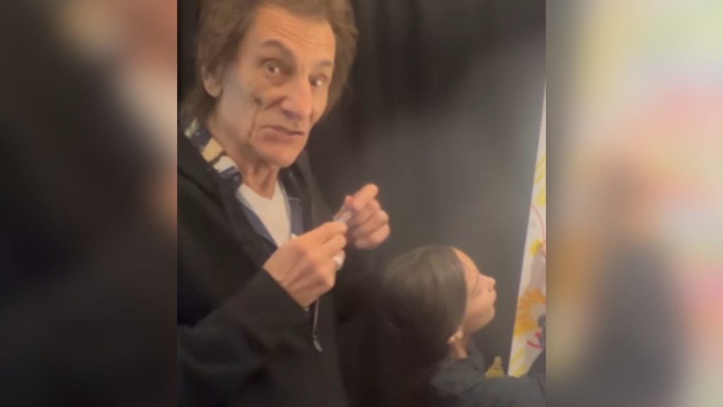 Ronnie Wood looks at the camera, eyes wide, as he holds a marker in his hands. Standing next to him is one of his twins. She's busy adding something to the setlist that's just out of view in this image