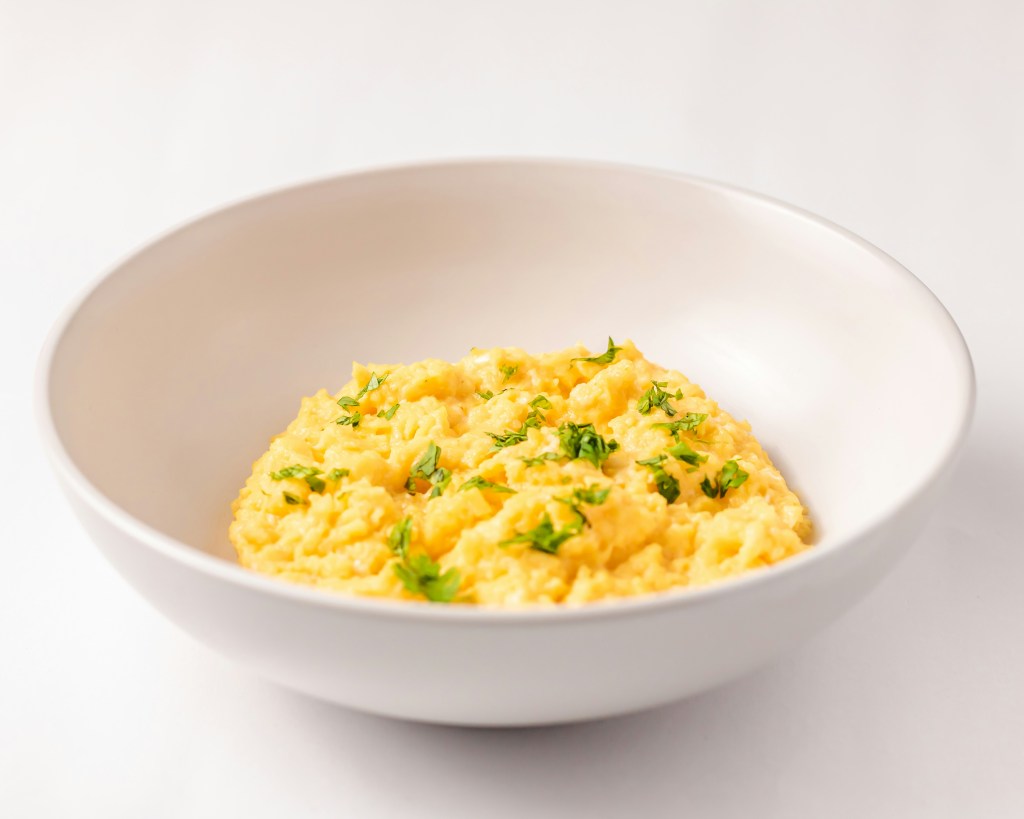 A bowl of scrambled eggs with herbs on top. 