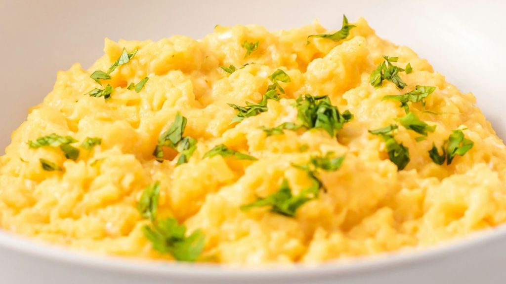 A bowl of scrambled eggs with herbs on top.