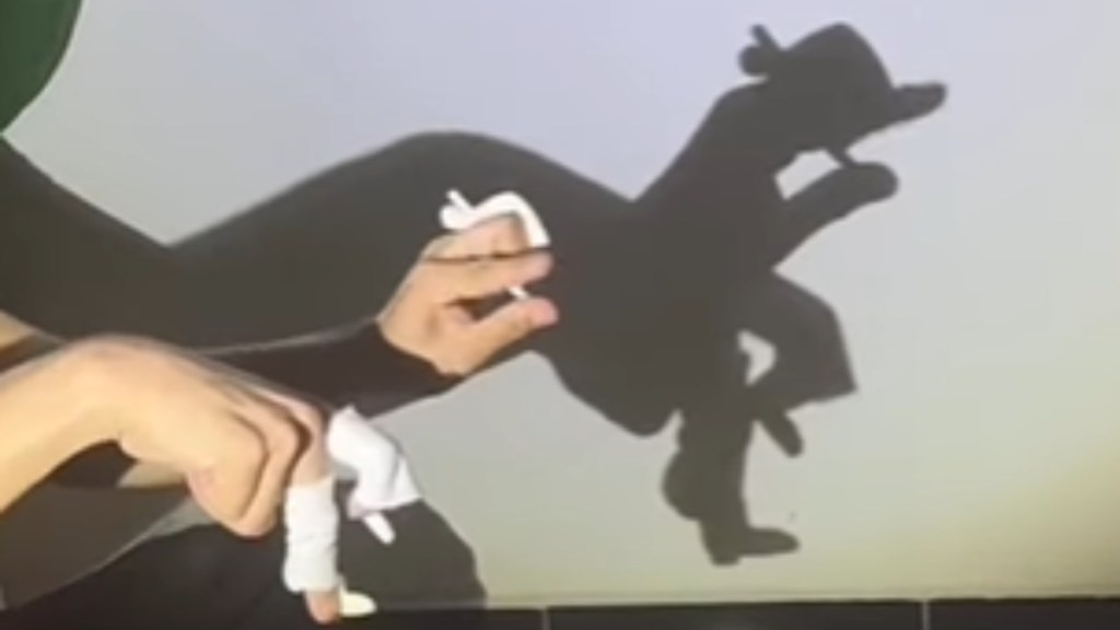 Close up of a shadow puppet artist's hands and the shadow they're making. The shadow appears like a man dancing