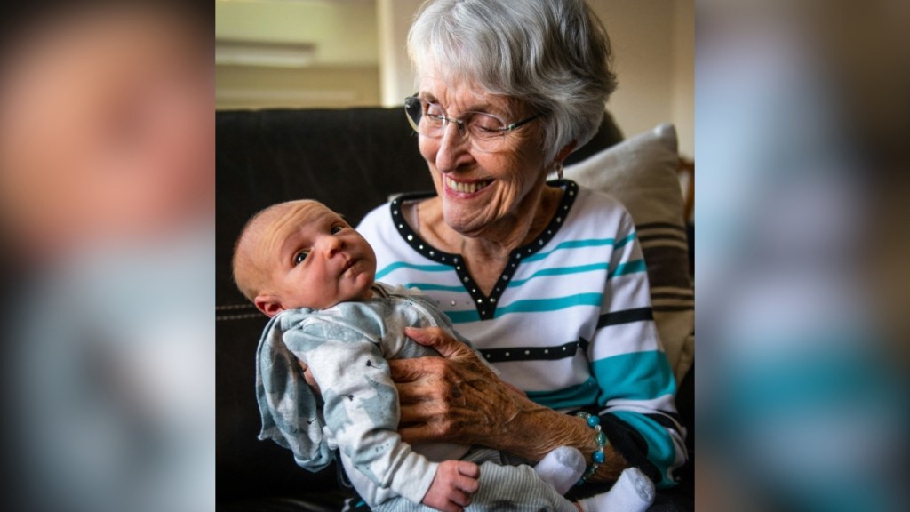 A grandma smiles wide as she looks down at the baby in her arms