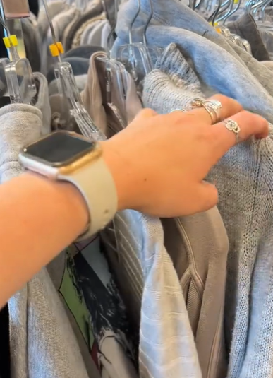A woman's hand browses through a clothes rack. 