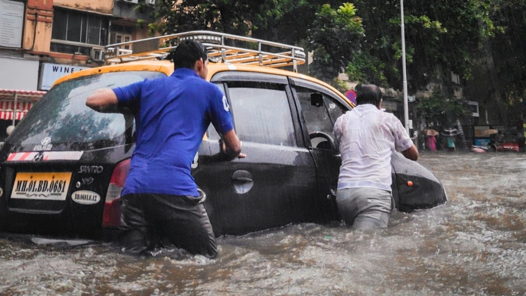 View from behind of two men pushing a car through flooded waters. The water is so high it reaches their knees and higher